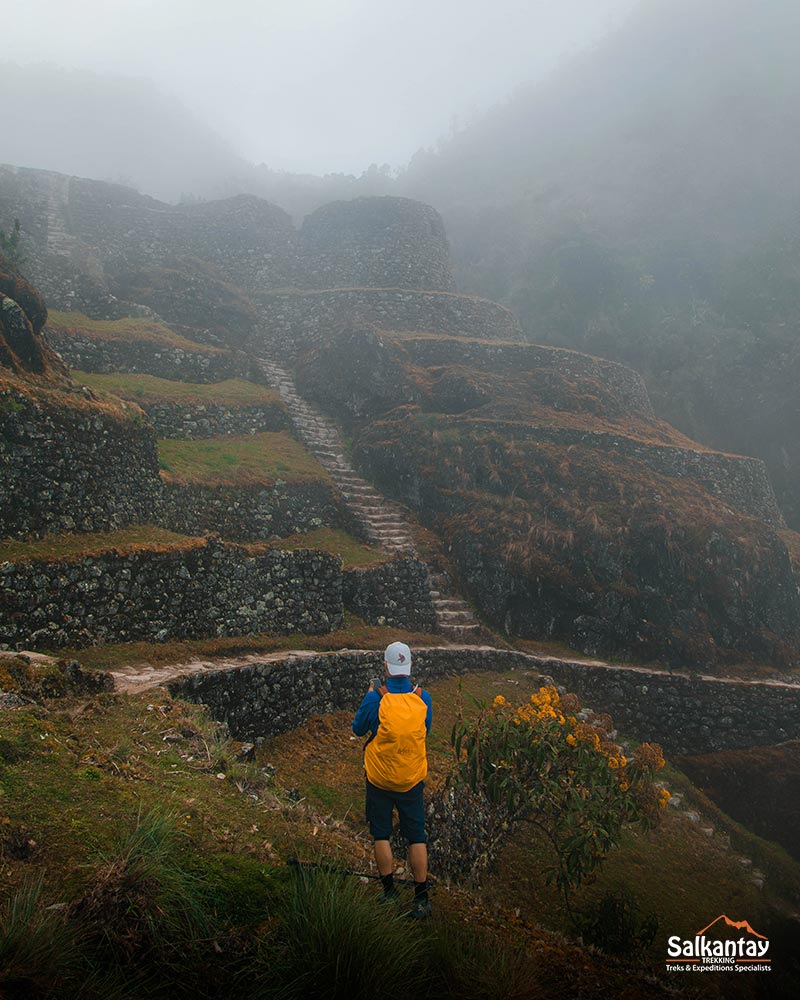 Turista con una mochila de color naranja en un sitio arqueológico del Camino Inca perdido en una inmensa niebla.