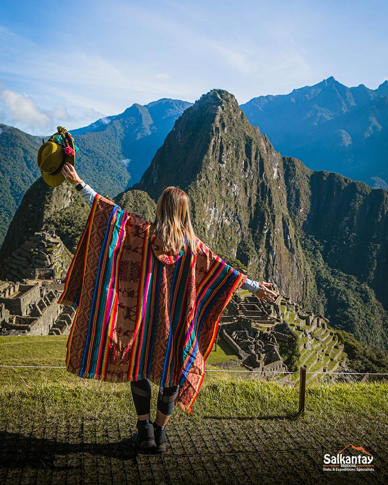 Turista mujer con poncho andino viendo Machu Picchu