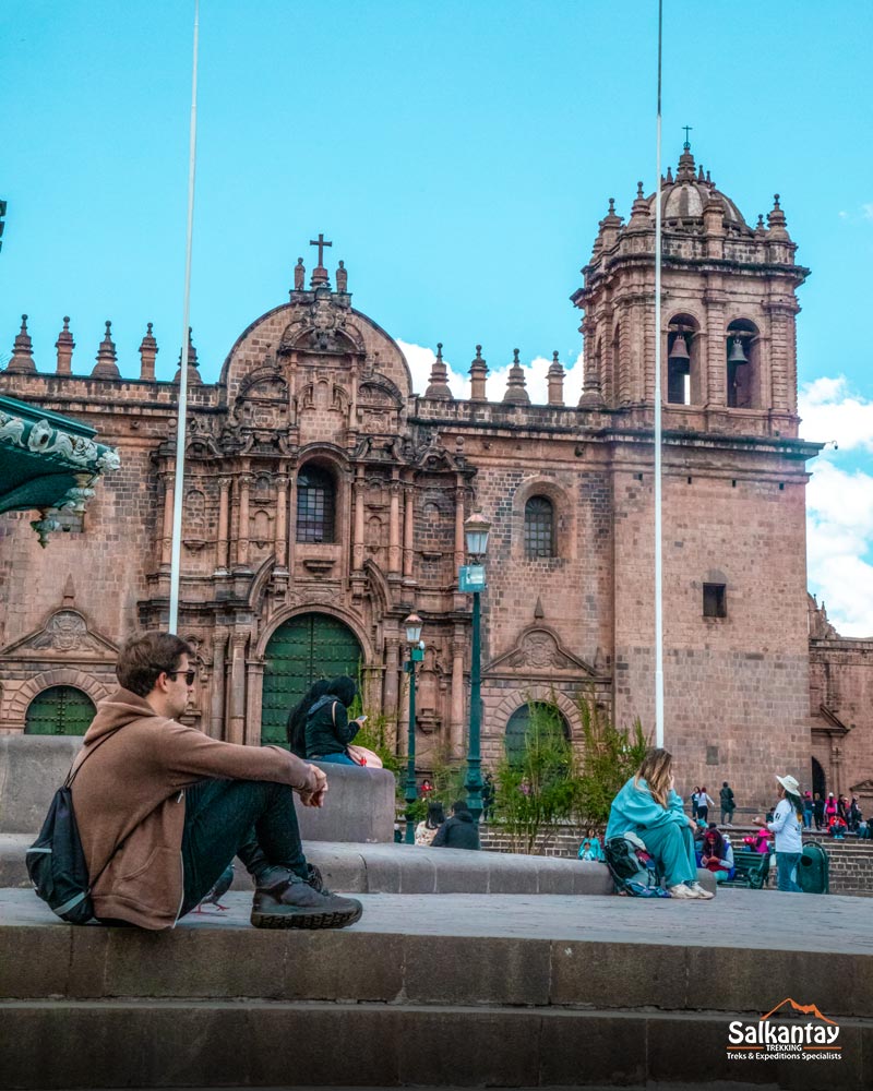 Turista sentado en la plaza principal de Cusco mirando la catedral