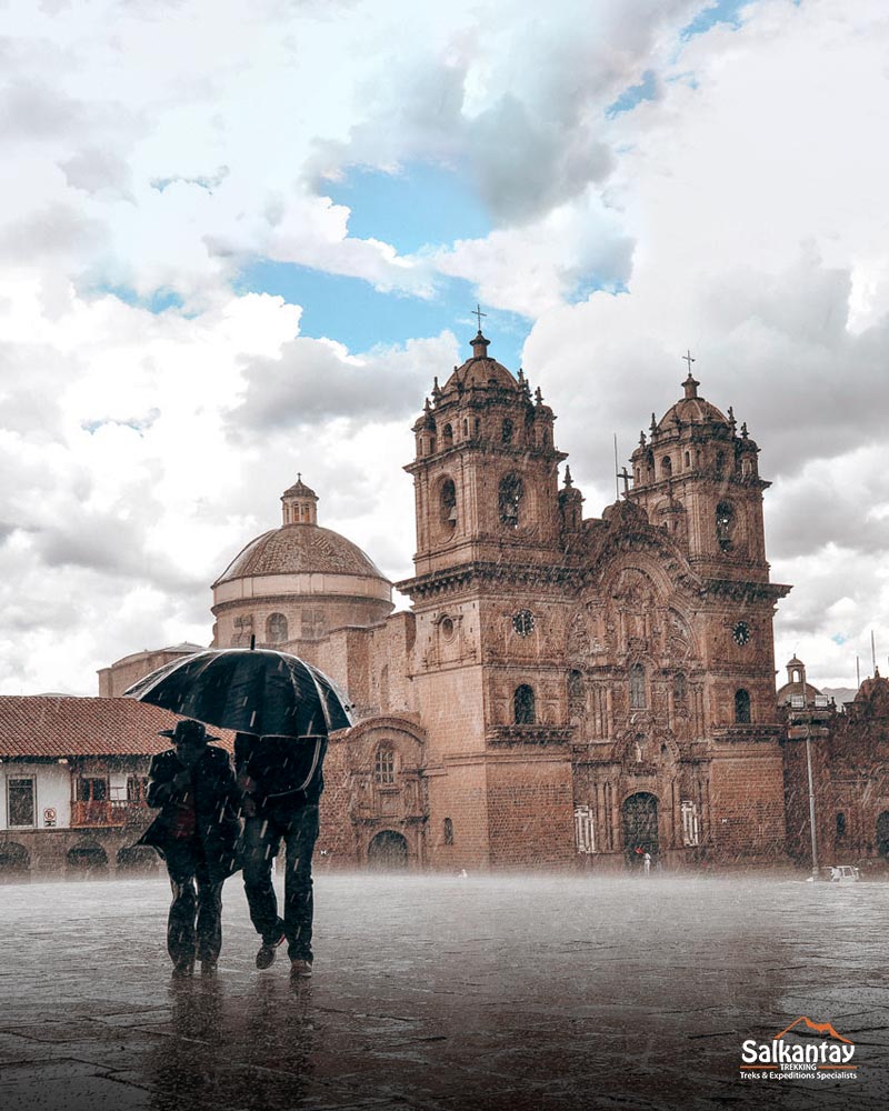 Dos turistas con paraguas en la plaza principal de Cusco bajo una lluvia torrencial