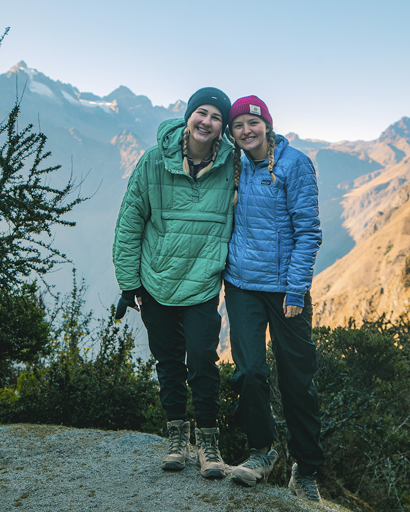 Dos turistas mujeres posando con el fondo de los paisajes que ofrece el Camino Inca a Machu Picchu