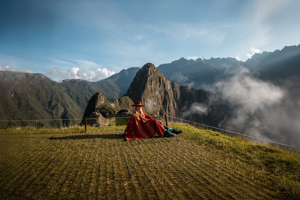 Turista con un poncho andino rojo con la ciudadela inca de Machu Picchu al fondo.