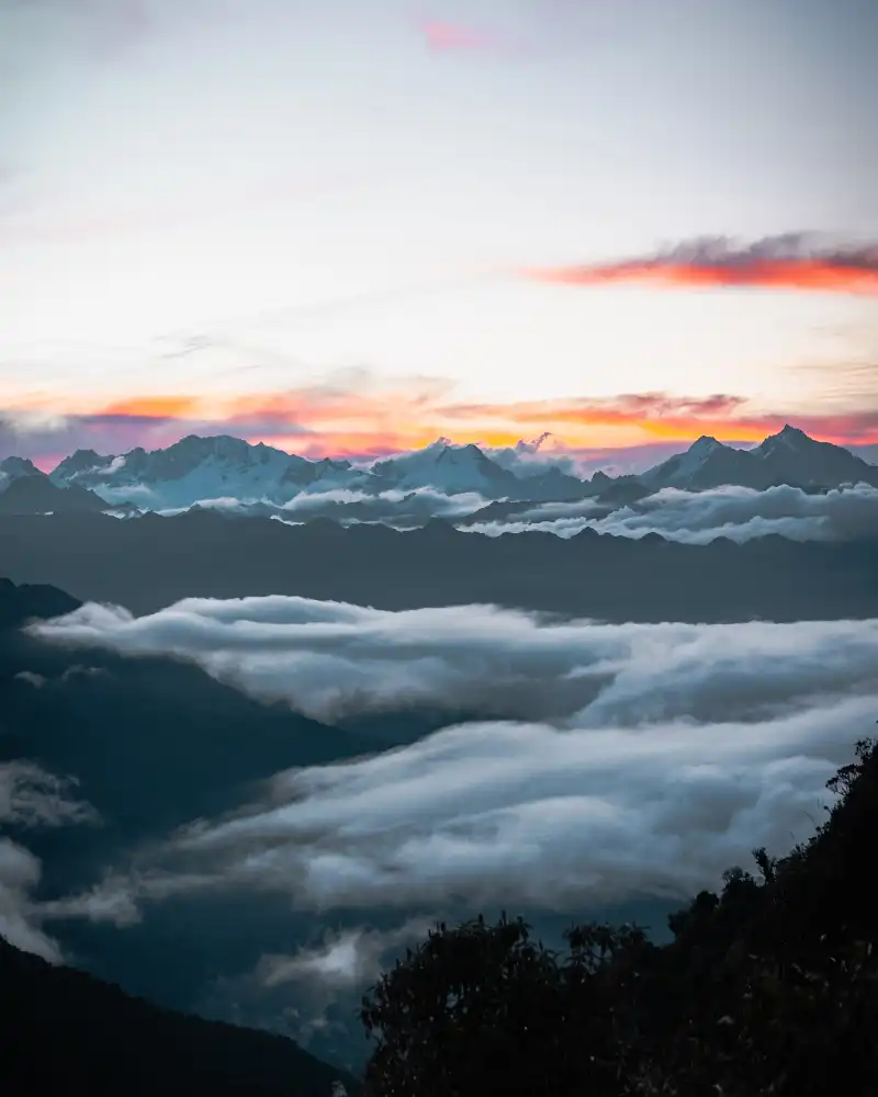 Amanecer en el Camino Inca con montañas nevadas de fondo, arcoiris en las nubes y la neblina cubriendo la vegetación
