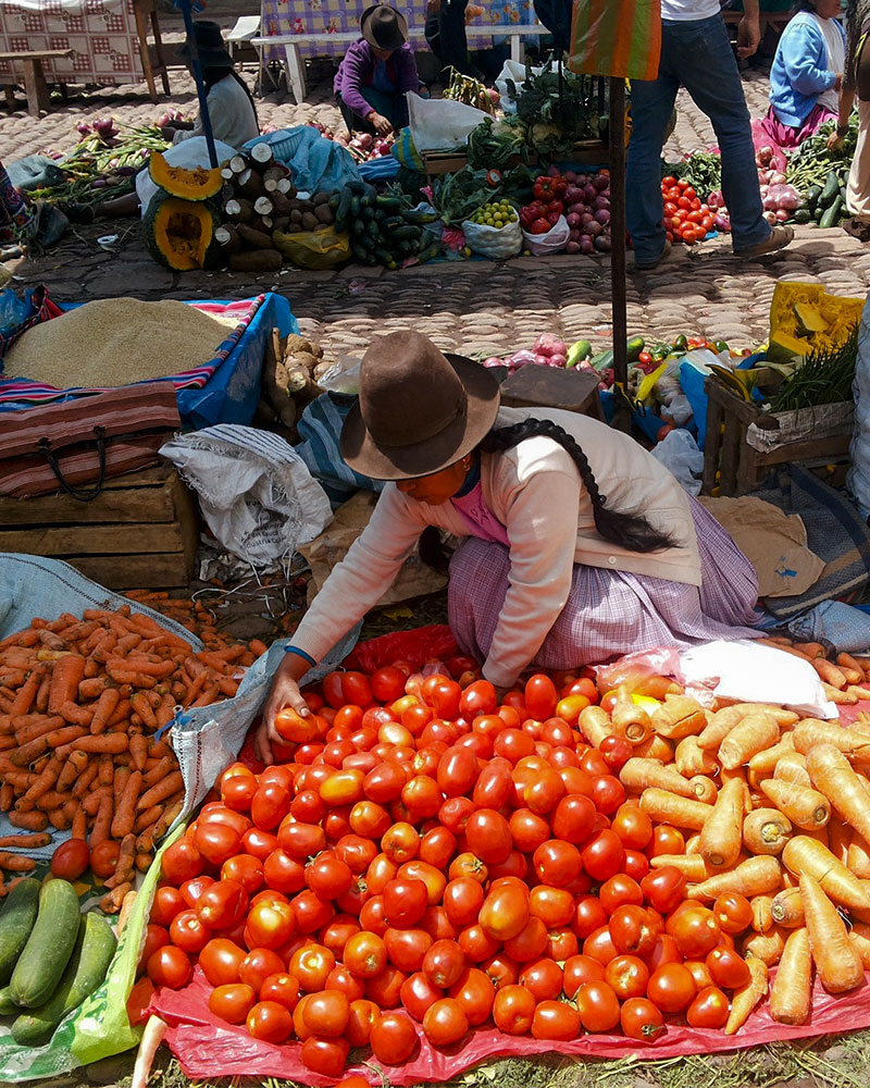 Señora vendiendo tomates y zanahorias en un mercado de Cusco