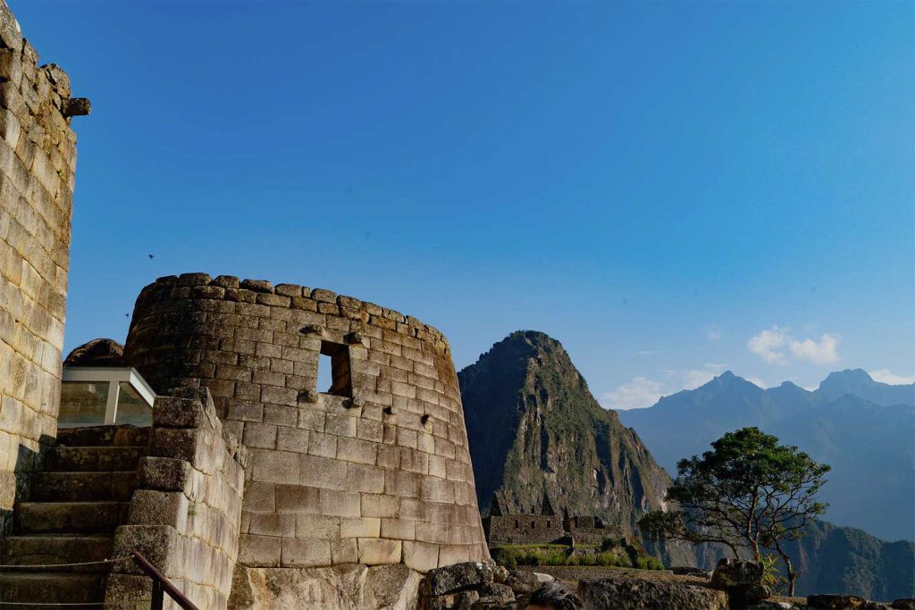 Fotografia del Templo del Sol en Machu Picchu, tomada desde afuera, con la montaña Huayna Picchu de fondo, en un día de sol