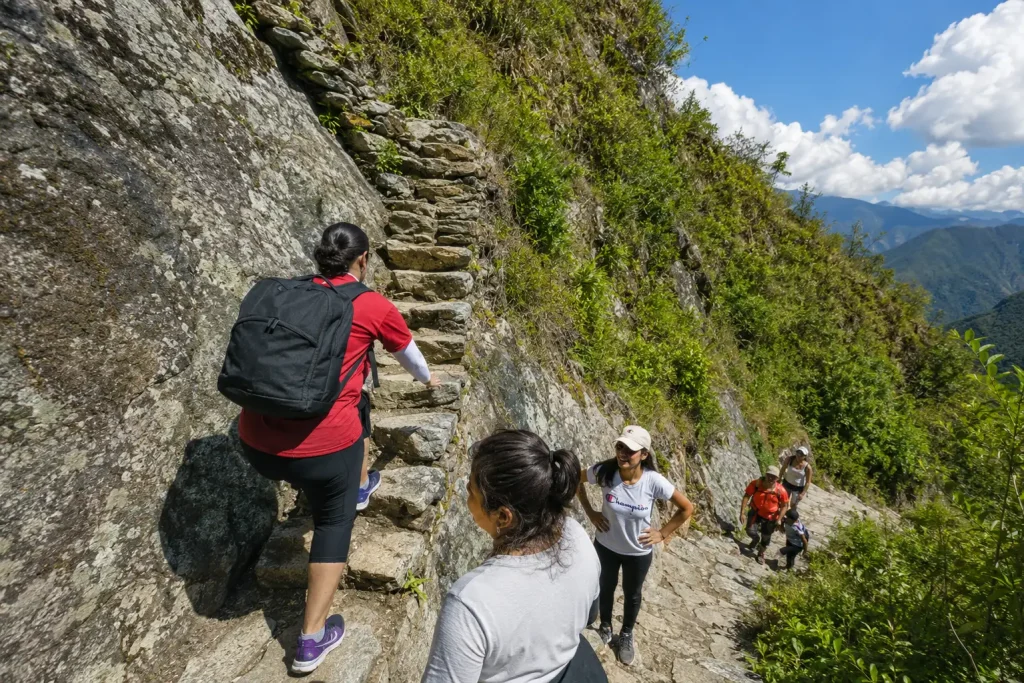 Excursionistas subiendo las empinadas escaleras de piedra incas rodeadas de exuberantes montañas verdes en el Camino Inca.