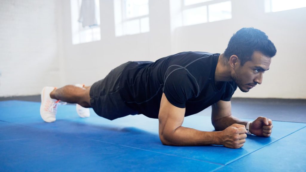 Una persona en posición de plancha sobre los antebrazos sobre una colchoneta azul durante un entrenamiento de abdominales.