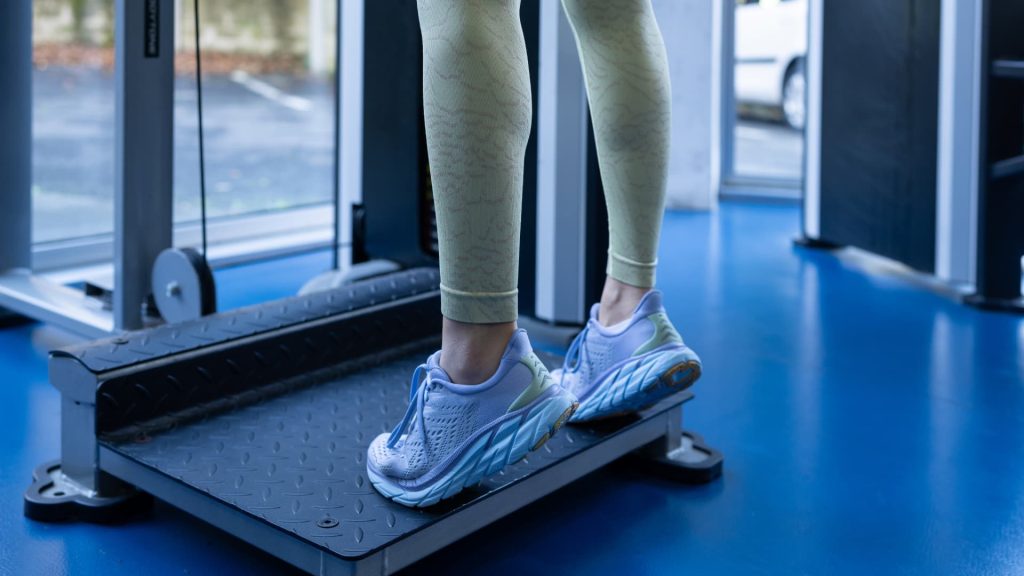 Primer plano de una persona realizando elevaciones de pantorrillas de pie sobre una plataforma elevada en un gimnasio.