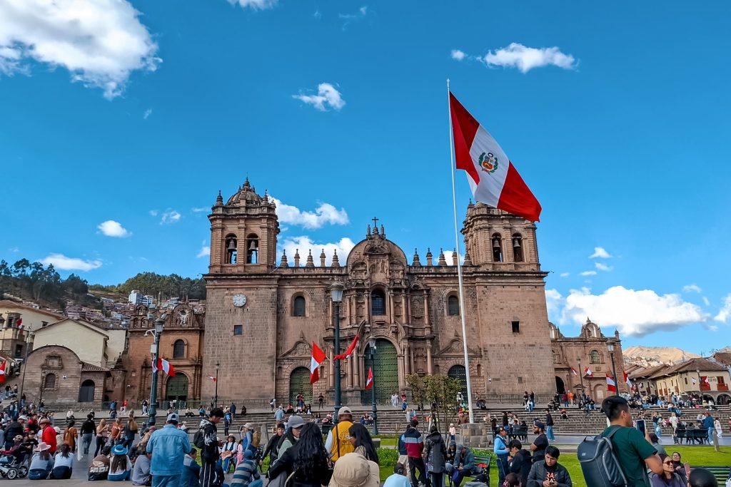 Plaza de armas de Cusco lleno de personas con una bandera de Perú flameando