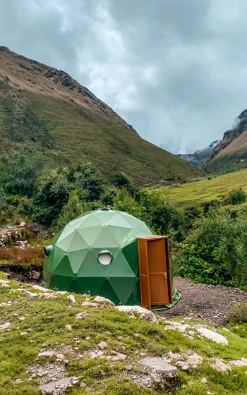 Un moderno domo geodésico en el campamento Salkantay Mountain Domes en Soraypampa, diseñado para el confort con un ventanal panorámico frente a los majestuosos picos andinos nevados.
