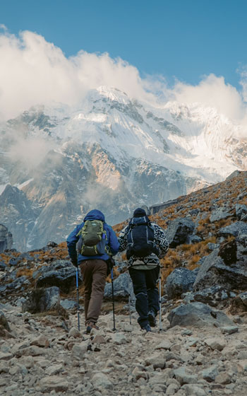 Dos turistas caminando en la ruta del Salkantay Trek, con la impresionante cumbre nevada de la Montaña Salkantay al fondo.