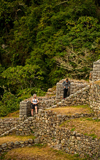 Dos turistas en el sitio arqueológico de Wiñay Wayna durante la caminata por el Camino Inca, rodeados de impresionantes terrazas incas y paisajes andinos.