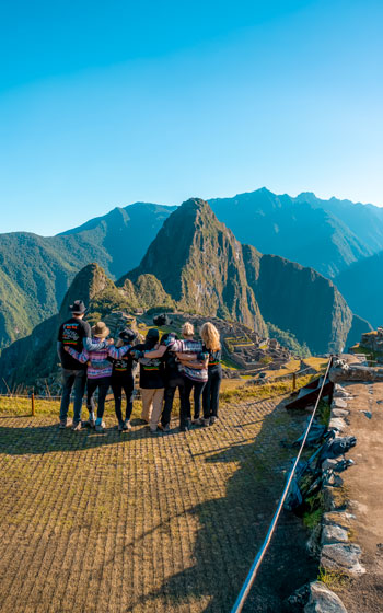 Gran grupo de turistas felices y abrazándose en el mirador, admirando la impresionante vista panorámica de Machu Picchu, Perú.