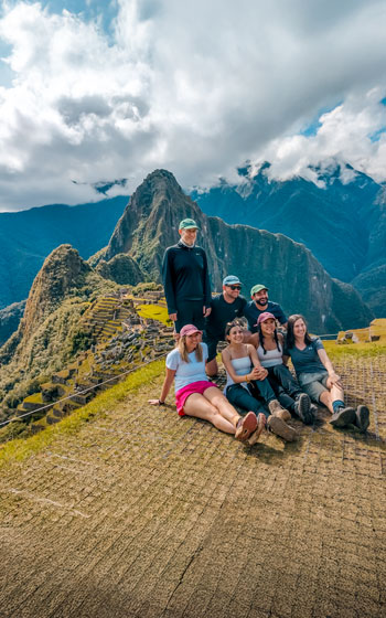 Grupo de turistas sonriendo y posando en la antigua Ciudadela Inca de Machu Picchu, disfrutando del impresionante paisaje y la rica herencia de Perú.