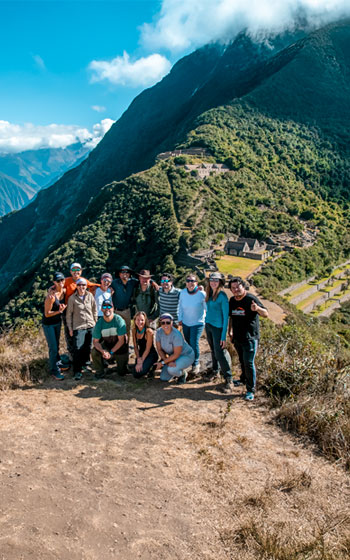 Grupo de turistas posando con el sitio arqueológico de Choquequirao como impresionante fondo, destacando la escala del lugar.