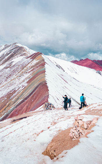 Grupo de turistas posando frente a la Montaña de Siete Colores (Vinicunca), cuya cima está parcialmente cubierta de nieve en los Andes de Perú.