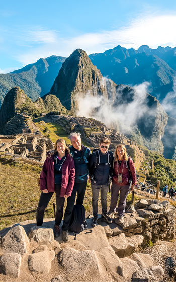 Grupo de turistas posando con la majestuosa Ciudadela de Machu Picchu de fondo, disfrutando del impresionante paisaje y el rico patrimonio cultural de Perú.