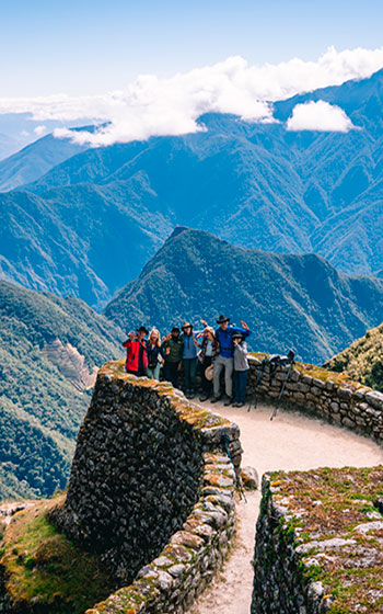 Grupo de turistas en el sitio arqueológico de Phuyupatamarka durante el Camino Inca, rodeados de impresionantes paisajes andinos y arquitectura ancestral.
