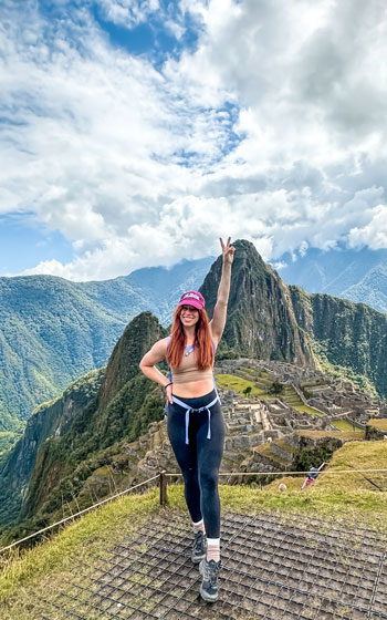 Mujer turista celebrando con las manos en alto en la antigua Ciudadela Inca de Machu Picchu, capturando la energía y la belleza de Perú.