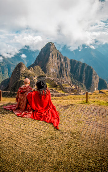Pareja de turistas con ponchos andinos coloridos admirando la maravilla de Machu Picchu, rodeada por las majestuosas montañas de Perú.