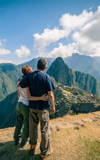 Pareja de turistas abrazados mientras contemplan la impresionante ciudadela inca de Machu Picchu, rodeada de montañas andinas y un paisaje histórico único.