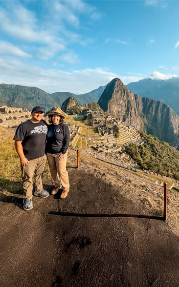 Pareja de turistas admira el magnífico sitio arqueológico de Machu Picchu, rodeado de exuberantes montañas y la mística belleza de los Andes peruanos.