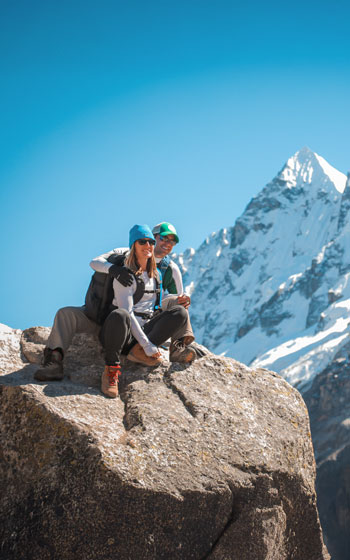 Pareja de turistas sentada sobre una roca con el imponente nevado Salkantay de fondo, disfrutando del majestuoso paisaje andino del Perú.