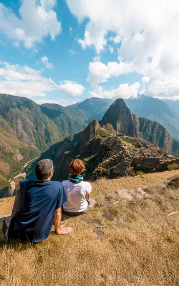 Pareja de turistas contemplando la vista panorámica de la ciudadela inca de Machu Picchu, rodeada de montañas y un impresionante paisaje andino.