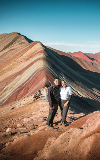 Pareja de turistas celebrando en la cima de la famosa Montaña Arcoíris (Vinicunca), un destino clave en Cusco.
