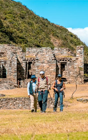 Tres turistas explorando las ruinas y terrazas del inmenso sitio arqueológico de Choquequirao.