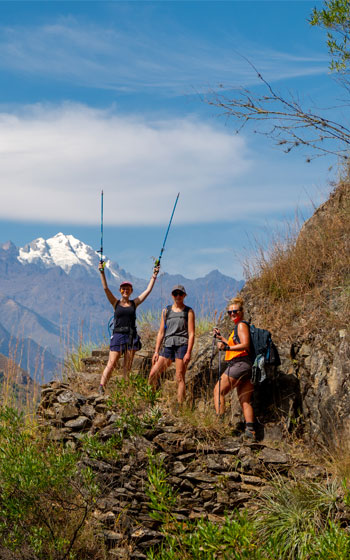 Tres turistas posando en el ruta Inca Jungle, con las majestuosas montañas de los Andes como fondo, disfrutando de la aventura en Perú.