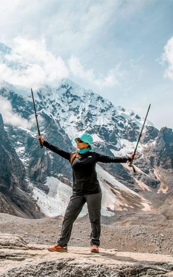 Turista celebrando con las manos en alto y bastones de trekking en el Paso Salkantay, el punto más alto de la ruta Salkantay Trek.