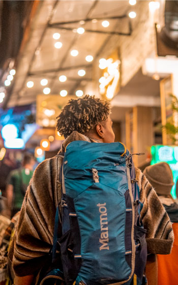 Turista caminando por las calles de Aguas Calientes, también conocido como Machu Picchu Pueblo, rodeado de su ambiente turístico y el paisaje andino.