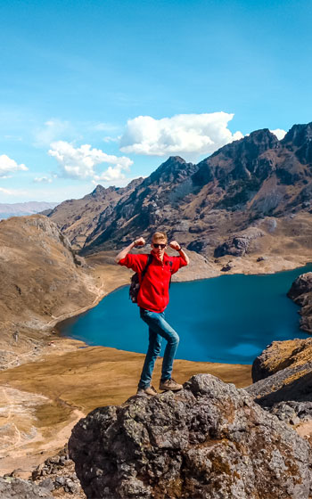 Turista de pie frente a la impresionante laguna turquesa de Lares, capturando la pacífica belleza y el encanto de los Andes peruanos.
