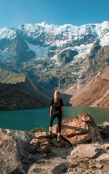Turista posando frente a las aguas turquesas de la Laguna Humantay y la imponente Montaña Humantay en Cusco.