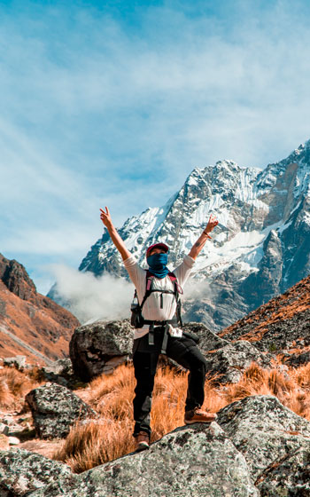 Turista celebrando con las manos en alto frente a la imponente y nevada cumbre de la Montaña Salkantay en el trekking.