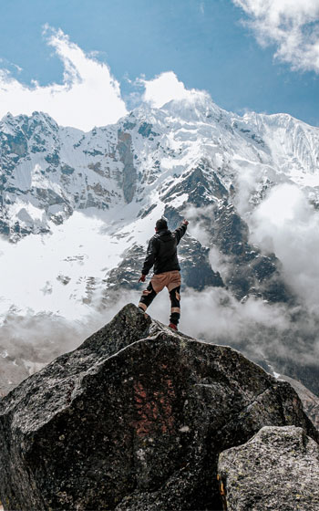 Turista levantando las manos en señal de logro frente a la Montaña Sagrada de Salkantay. Trekking de alta montaña y vistas al nevado en Perú.