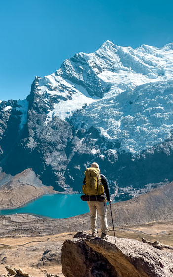 Turista con mochila de pie frente al majestuoso nevado Ausangate, la montaña sagrada más importante de la Cordillera de los Andes de Perú.
