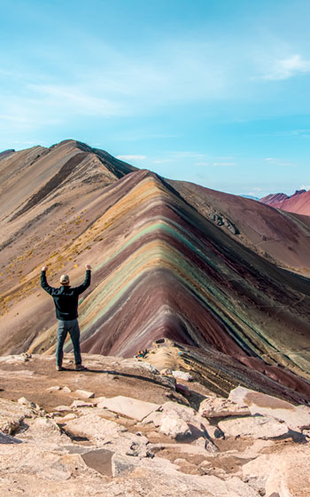 Turista levantando las manos en señal de alegría frente a la Montaña de Siete Colores (Vinicunca), capturando la energía de Perú.