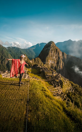 Turista mujer con poncho rojo posando en la icónica Ciudad Inca de Machu Picchu.