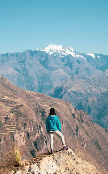 Turista disfrutando de la vista panorámica de las majestuosas montañas andinas en la ruta Huchuy Qosqo, reflejando la tranquilidad de la sierra peruana.
