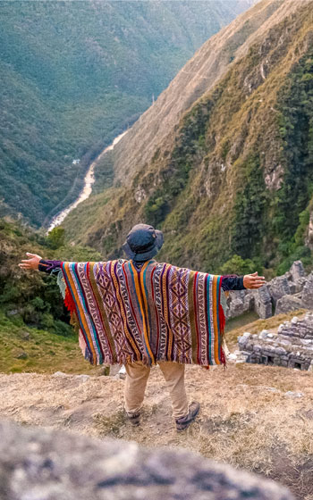 Turista con poncho andino en las terrazas del sitio arqueológico de Wiñay Wayna, una parada clave en el famoso Camino Inca.