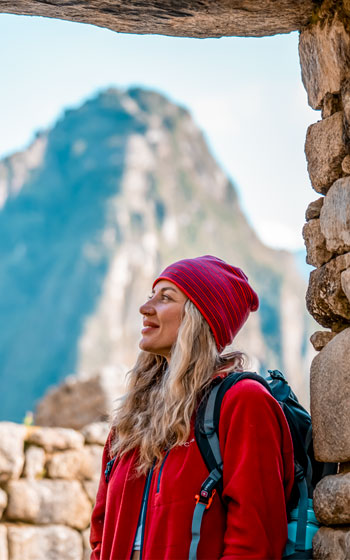Turista en una portada o puerta inca con la imponente montaña Huayna Picchu de fondo, apreciando el paisaje andino y la arquitectura ancestral.