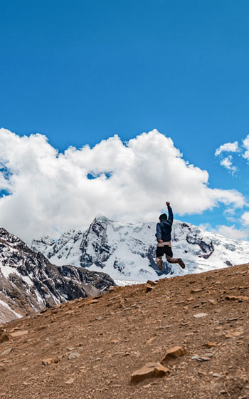 Turista saltando de alegría en el Paso Palomani, a más de 5.200 metros sobre el nivel del mar. Nevado Ausangate de fondo. Logro de trekking de alta montaña en Perú.