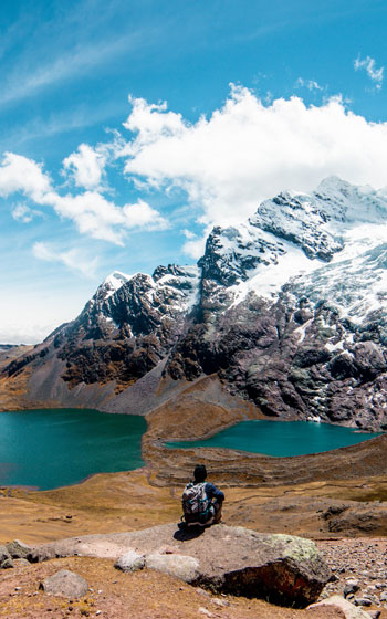 Turista sentado admirando el majestuoso nevado Ausangate, rodeado de imponentes montañas y la belleza natural de los Andes peruanos.