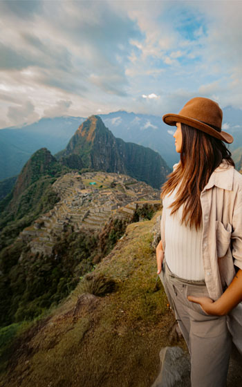 Turista con sombrero andino, contemplando la impresionante ciudadela inca de Machu Picchu rodeada de montañas y un paisaje andino majestuoso.