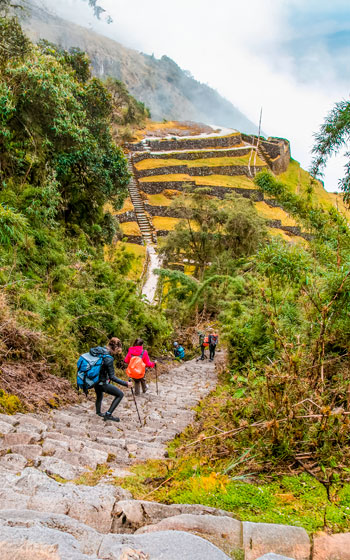 Turistas caminando hacia el sitio arqueológico de Phuyupatamarka en el Camino Inca, rodeados de paisajes andinos espectaculares.