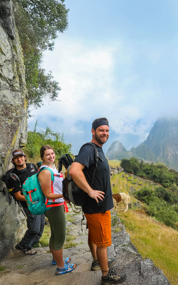 Turistas y su guía ingresan a Machu Picchu por la icónica ruta de la Puerta del Sol (Intipunku), disfrutando de impresionantes vistas panorámicas de la antigua ciudad inca y los Andes circundantes.
