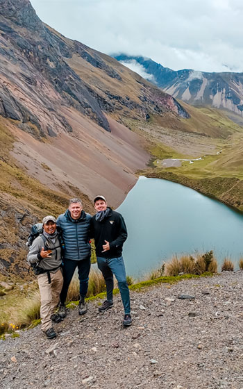 Dos turistas y su guía disfrutan un momento escénico con la hermosa laguna Ancascocha de fondo, rodeada por los majestuosos picos de los Andes peruanos.