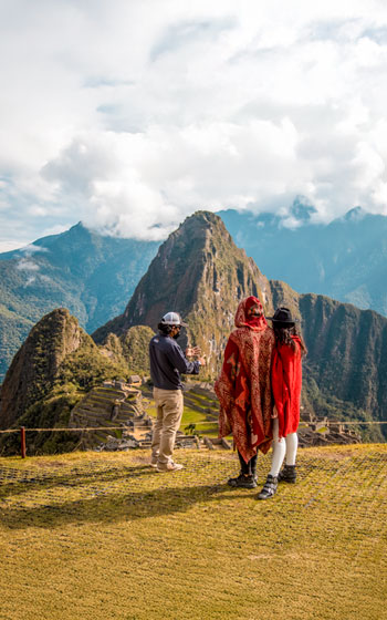 Guía y grupo de turistas con ponchos rojos posando en un tour frente a la icónica ciudadela Inca de Machu Picchu.